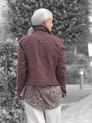 Person von hinten auf einem Weg, trägt die OFF#DLY Jacke Bologna schoko. Die Jacke ist tailliert mit Fransendetails und kombiniert Denim-Eleganz, über einem längeren Leoparden-Top und hellen Hosen.