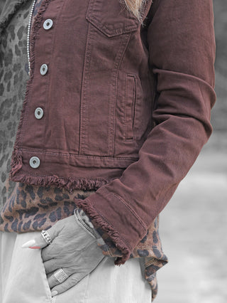Nahaufnahme der OFF#DLY Jacke Bologna schoko, getragen über einem Leopardenmuster-Top. Die Jacke zeigt fransige Säume und Ärmelabschlüsse, während eine Hand in einer hellen Hosentasche ruht.