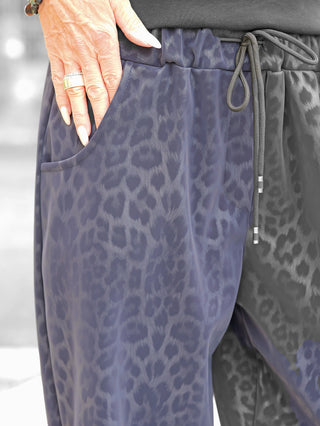 Nahaufnahme der OFF#DLY Leo Pant Freija blue, locker geschnittene Leopardenmuster-Hose mit elastischem Bund und Kordelzug, Taschen, getragen mit Ringen und langen, gepflegten Nägeln sichtbar.