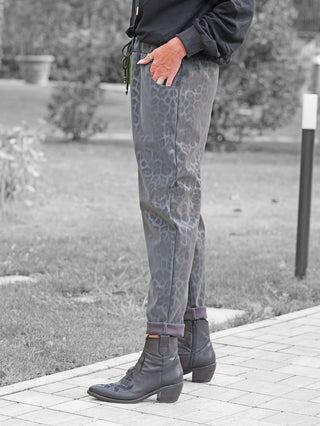 Die OFF#DLY Leo Pant Freija grey zeigt einen modernen Leo-Print in schlankem Schnitt, kombiniert mit schwarzen Lederstiefeln, die durch dekorative Nähte und einen niedrigen Absatz auffallen.