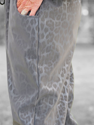 Nahaufnahme der OFF#DLY Leo Pant Freija grey mit grauem Leo-Muster. Hand steckt in Seitentasche, betont die lockere, seidige Textur und den elastischen Bund dieser modischen Hose.