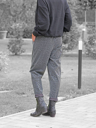 OFF#DLY Leo Pant Freija grey mit subtilen Leopardenmuster und elastischem Bund, getragen von einer Person auf einem Weg, kombiniert mit schwarzen Lederstiefeletten und einer lockeren schwarzen Jacke.