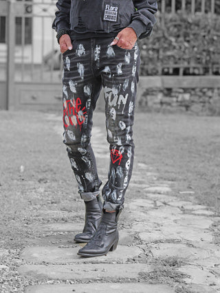 OFF#DLY Denim Donatella black/red: Schwarze Jeans mit weißem Farbspritzern und roten Graffiti-Mustern, umgekrempelte Säume, kombiniert mit schwarzen Lederstiefeletten und einem Sweatshirt mit Flora Move the Crowd-Patch.