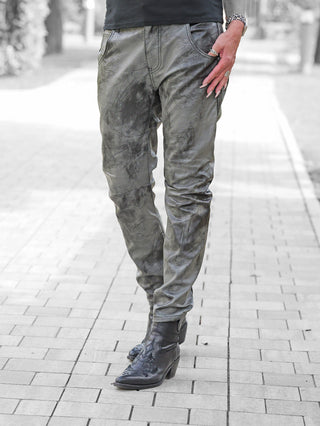 Person trägt OFF#DLY Fake Leather Denim Luna in grau, jogger-style, mit Lederoptik. Dazu schwarze, spitze Ankle Boots. Rechter Hand in Tasche mit Ringen und Uhr sichtbar, auf Gehweg stehend.