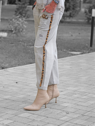 OFF#DLY Denim Mira grey Jeans mit schmalem Leo-Streifen an den Seitennähten, leicht destroyed Look. Person trägt sie mit nudefarbenen Stiletto-Stiefeletten, Hand in der Tasche, Ringe und Smartwatch sichtbar.