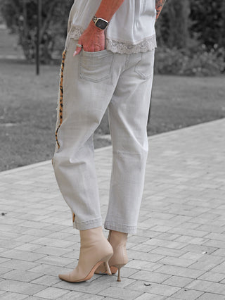 Person trägt OFF#DLY Denim Mira grey mit Leo-Streifen an den Nähten und leicht zerstörtem Look, kombiniert mit spitzen beigen Stiefeletten und weißem Spitzen-Top. Rechte Hand in der Gesäßtasche.