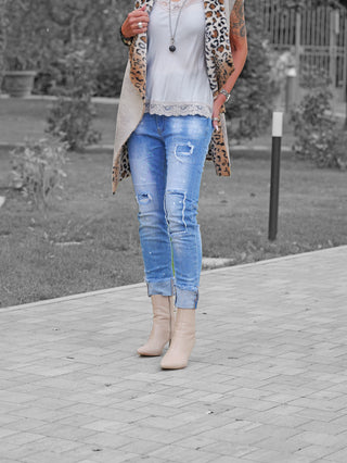Person trägt OFF#DLY Denim Lara lightblue: Distressed-Jeans mit Rissen und Farbdetails, kombiniert mit beigem Stiefeletten, weißem Spitzen-Top und Leopardenweste. Accessoires und Tätowierung sichtbar.