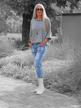 Eine Frau trägt das OFF#DLY Tee Tove grey, ein lässiges, oversized T-Shirt mit weiten Ärmeln, kombiniert mit hellen Jeans und hohen Schnürstiefeln, ideal für einen entspannten Alltagslook.