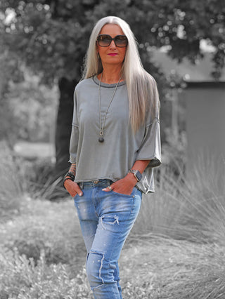 Frau trägt das OFF#DLY Tee Tove grey in einem lockeren, oversized Schnitt mit weiten Ärmeln. Kombiniert mit zerrissenen Jeans, ergänzt durch eine lange Kette und Armbänder.