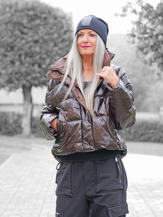 Die OFF#DLY Winterjacke Cortina schoko zeigt eine Frau im Freien mit grauem Haar, die eine glänzende Pufferjacke mit Leopardenmuster trägt, ideal für kalte Tage.