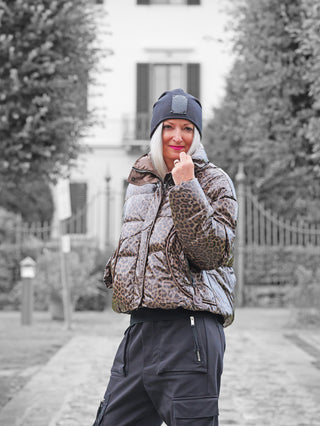 Eine Frau trägt die OFF#DLY Winterjacke Cortina taupe mit modernem Leopardenmuster auf einem steinernen Weg. Die Jacke ist eine glänzende, kurz geschnittene Pufferjacke, kombiniert mit schwarzen Cargo-Hosen.