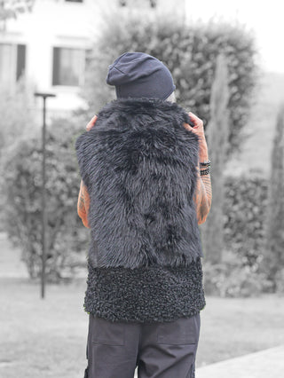 Person mit dem Rücken zur Kamera trägt die OFF#DLY Fell Imitat Weste Gröden black, kombiniert aus glattem und lockigem Kunstfell, über dunkler Hose, hebt Arme, um Beanie anzupassen.