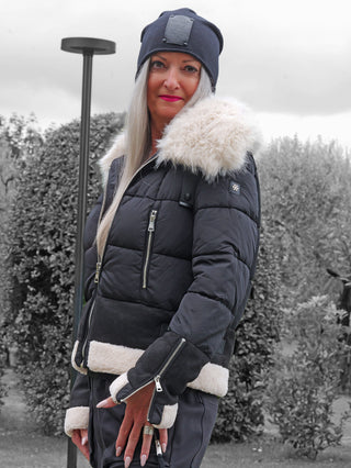 Frau trägt die OFF#DLY Jacke Canazei black, eine schwarze, gesteppte Winterjacke mit cremefarbenem Kunstfell an Kragen, Saum und Ärmelenden, kombiniert mit eingearbeiteten Reißverschluss-Fäustlingen.