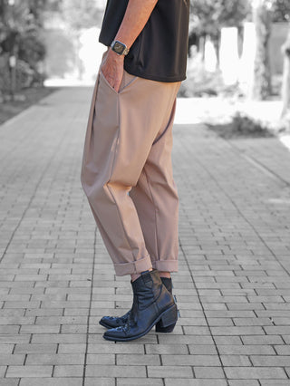 Person trägt OFF#DLY Baggy Pant Leyla beige mit lockerem, umgeschlagenem Saum. Hand in Tasche, zeigt lässigen Stil. Kombination aus Komfort und modernem Chic, betont durch schwarze Stiefeletten.
