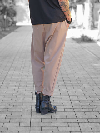 Person trägt OFF#DLY Baggy Pant Leyla beige mit umgeschlagenen Säumen, kombiniert mit schwarzen Lederstiefeletten. Sichtbare Details: lockere Passform, verkürztes Bein, lässige Eleganz. Beaded Armbänder und tätowierter Unterarm sichtbar.