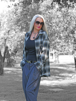 Frau trägt OFF#DLY Checker Bluse Amelia black/grey, offen über schwarzem Top, kombiniert mit blauer Hose. Die Bluse zeigt modernes Karomuster, locker geschnitten mit Kragen, Knopfleiste und Brusttasche.
