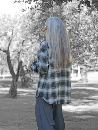 Person im Freien trägt die OFF#DLY Checker Bluse Amelia black/grey: eine lässig geschnittene, langärmlige Karo-Bluse mit Kragen und Brusttasche, kombiniert mit weiten Hosen.