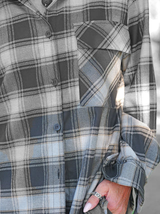 Nahaufnahme einer Person, die die OFF#DLY Checker Bluse Amelia black/grey trägt, mit graublau-karierter Musterung, Knopfleiste, Brusttasche und hochgekrempeltem Ärmel, ergänzt durch silberne Ringe und eine Kette.