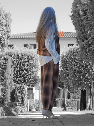Person von hinten vor Villa im OFF#DLY Weste Alison braun checker, kombiniert mit passender Hose. Die Weste zeigt ein modernes Karo-Design, ideal für trendige Layering-Looks, rundet das Outfit stilvoll ab.