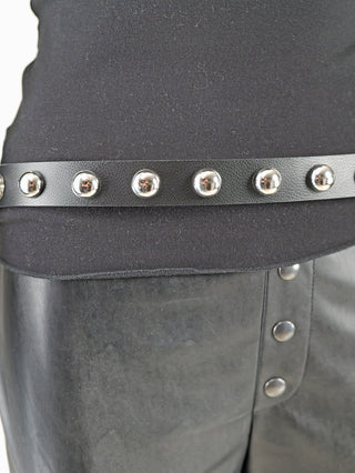 Nahaufnahme eines schwarzen OFF#DLY Gürtel Leder silver Ball black mit silbernen Halbkugel-Nieten, getragen über einem schwarzen Oberteil, das in einen mattschwarzen Rock oder Hose mit silbernen Druckknöpfen gesteckt ist.
