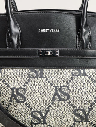 Sweet Years Logo Bag black: Nahaufnahme einer Tasche mit schwarzem Leder und Metalllogo oben, geometrischem SY-Muster auf hellem Canvas unten, und einem kleinen Drehverschluss an einem Lederriemen.