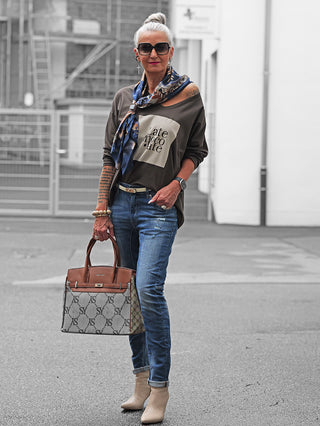 Die stilvoll gekleidete Frau trägt die OFF#DLY Denim Bergamo midblue, eine schmal geschnittene, leicht zerstörte Jeans, kombiniert mit beigen Stiefeletten und einem braunen Ledergürtel.