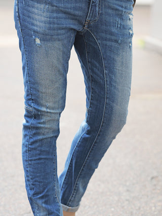 Beine in schmal geschnittener OFF#DLY Denim Bergamo midblue Jeans mit Used-Look, kleinen Rissen und Fading, stehend auf dem Gehweg.