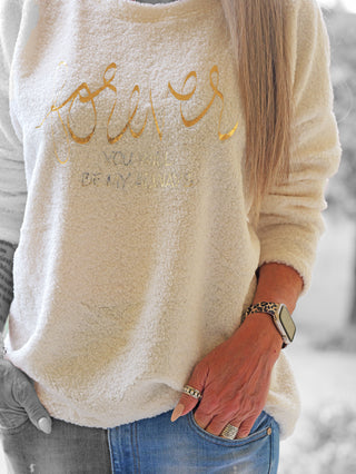 Träger in OFF#DLY Teddy Shirt beige mit goldener Schrift „forever“, kombiniert mit blauer Jeans. Sichtbare Details: Smartwatch mit Leopardenarmband, lange Nägel, Ringe. Kuscheliger Stil für kühle Tage.