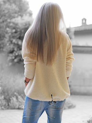 Eine Person trägt das OFF#DLY Teddy Shirt beige, ein kuscheliges, sherpa-artiges Oberteil, kombiniert mit blauen Jeans. Das Shirt hat eine lockere Passform und bietet gemütlichen Tragekomfort.