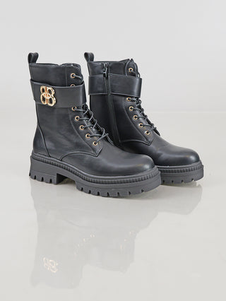 OFF#DLY Boot BB/L black: Schwarze Schnürboots mit klobiger Plateausohle, seitlichem Reißverschluss, dekorativem Knöchelriemen mit goldener Schnalle, aus Polyurethan, auf glatter Oberfläche präsentiert.
