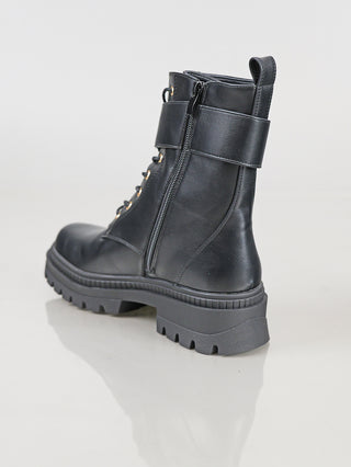 OFF#DLY Boot BB/L black: Schwarzer Combat-Boot mit mattem Leder, seitlichem Reißverschluss, Klettverschluss-Riemen, grober Gummisohle, unlackierten Metallösen und Fersenlasche, auf glänzender Fläche leicht angewinkelt positioniert.