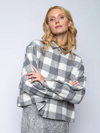 Emily Bluse Checker grey/white: Frau trägt eine übergroße, grau-weiß karierte Hemdbluse mit XXL-Tasche und locker gefalteten Ärmeln. Kombiniert mit einem grauen, texturierten Bouclé-Rock oder Hose.