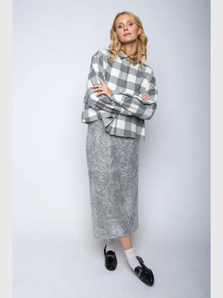 Die Emily Bluse Checker grey/white zeigt ein grau-weiß kariertes Design mit lockerer Passform und einer XXL-Tasche, getragen von einer blonden Frau mit gekreuzten Armen und neutralem Ausdruck.