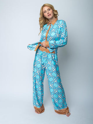Emily Hose 201238 cognac: Modell trägt hellblaues Loungewear-Set mit abstraktem Muster und orange-weißen Akzenten, bestehend aus langärmligem Oberteil und weit geschnittener Hose, aus fließendem Viskose-Satin.