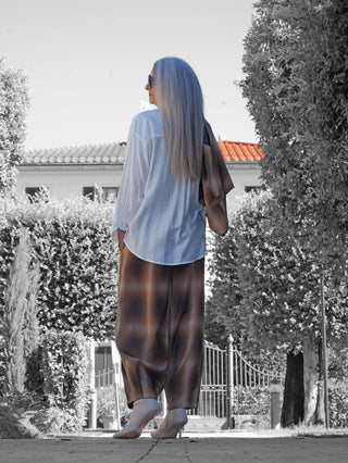 Die OFF#DLY Bluse Pordoi white, getragen von einer Person, zeigt eine elegante weiße, fließende Passform aus Rayon, kombiniert mit einer weiten, karierten Hose, die über die Schulter getragen wird.