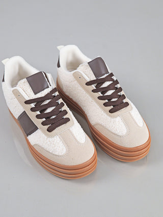 OFF#DLY Sneaker Roma beige mit dicker Gummisohle, beige Wildleder-Panels und weißem, flauschigem Obermaterial. Dunkelbraune Schnürsenkel und passendes Leder-Zungenpatch, auf grauem Hintergrund platziert.