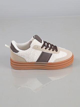 OFF#DLY Sneaker Roma beige aus sherpa-ähnlichem Material mit beigen Wildlederakzenten, dunkelbraunem Streifen und Schnürsenkeln, auf einer dicken Gummisohle, auf einer glatten, hellgrauen Oberfläche präsentiert.