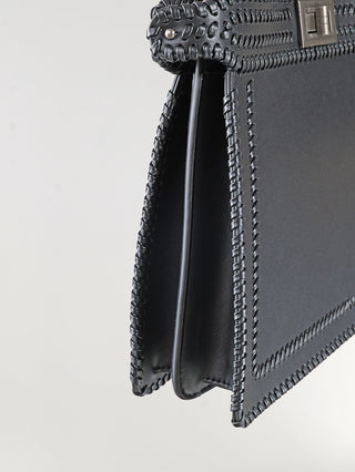 Off#DLY Bag black: Nahaufnahme einer kleinen strukturierten Henkeltasche aus schwarzem Leder mit dekorativer Peitschennähkante und einem Metall-Drehverschluss. Enthält einen langen Trageriemen. Maße: 33 x 25 x 8 cm.