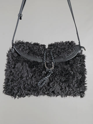 OFF#DLY Fake Fur Bag black aus schwarzem, lockigem Kunstfell mit passender Lederklappe, verstellbarem Lederriemen und geflochtener Lederschnur mit Metallring als Verschlussdetail. Größe: 36 x 27 x 7 cm.