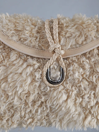 Nahaufnahme der OFF#DLY Fake Fur Bag beige, einer Henkeltasche mit flauschiger, wollähnlicher Oberfläche und glatter Lederbesatz. Verschluss mit geflochtener Lederschnur durch einen silbernen Metallring.
