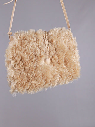 OFF#DLY Fake Fur Bag beige: Kleine Schultertasche aus hellbeigem Teddy-Material mit schmalem Lederband und geflochtenem Lederzugverschluss in der Mitte, ideal für stilvolle Akzente und funktionale Eleganz.