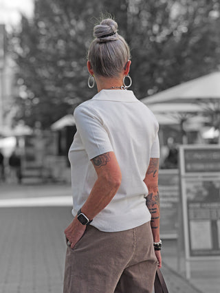 Person von hinten mit hochgestecktem grauem Haar trägt den OFF#DLY Polo Pulli creme mit Glitzersteinen, kombiniert mit braunen Cordhosen und silbernen Accessoires in urbanem Umfeld.