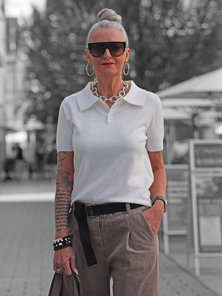 Silberhaarige Frau trägt OFF#DLY Polo Pulli creme mit Glitzersteinen, schmal geschnitten und sportlich-elegant, kombiniert mit weiten Cordhosen und Accessoires in urbaner Umgebung.