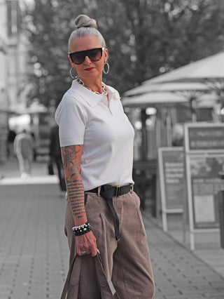 Frau trägt OFF#DLY Polo Pulli creme mit Glitzersteinen, kombiniert mit lockeren taupe Cordhosen und Accessoires, auf einer Einkaufsstraße.