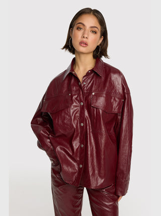 Eine junge Frau trägt die ALIX Fake Leather Bluse bordeaux, eine oversized Blusenjacke mit Cracked-Leather-Effekt, Brusttaschen und Knopfleiste, kombiniert mit passenden, gerade geschnittenen Hosen.