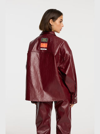 ALIX Fake Leather Bluse bordeaux: Model von hinten in bordeauxfarbenem Oversize-Jacke und passender Hose, mit drei Label-Patches am Rücken, großen silbernen Creolen, auf weißem Hintergrund.