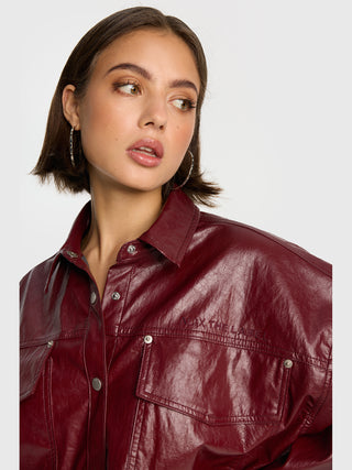 ALIX Fake Leather Bluse bordeaux, getragen von junger Frau, zeigt eine glänzende bordeauxrote Lederoptik mit Brusttaschen und dezentem Markenlogo. Der oversized Schnitt verleiht lässigen, modernen Style.