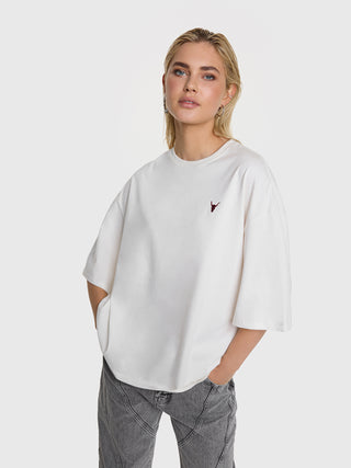 Eine junge Frau trägt das ALIX Back Logo Tee in soft white, mit kleinem Bullendetail vorne und großem Logo-Print hinten, kombiniert mit grauen Patch-Naht-Jeans.