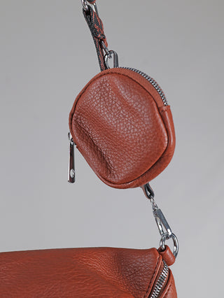 Nahaufnahme des OFF#DLY Crossbody Bag zimt mit kleiner runder Tasche. Zeigt texturiertes Leder, Reißverschluss und Metallclips, die die Tasche an der Haupttasche befestigen.