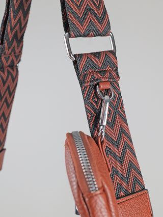 Nahaufnahme des OFF#DLY Crossbody Bag zimt mit abnehmbarem Schulterriemen. Chevron-Muster in Schwarz-Rost, silberner Haken und D-Ring, oberer Rand der braun-orangenen Tasche mit Reißverschluss sichtbar.